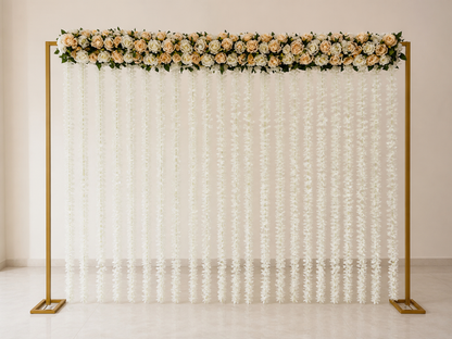 A nikah partition backdrop stand with a gold metal frame, decorated with a top floral garland of peach, cream, and white roses with green leaves, and hanging white lace flower curtains below.